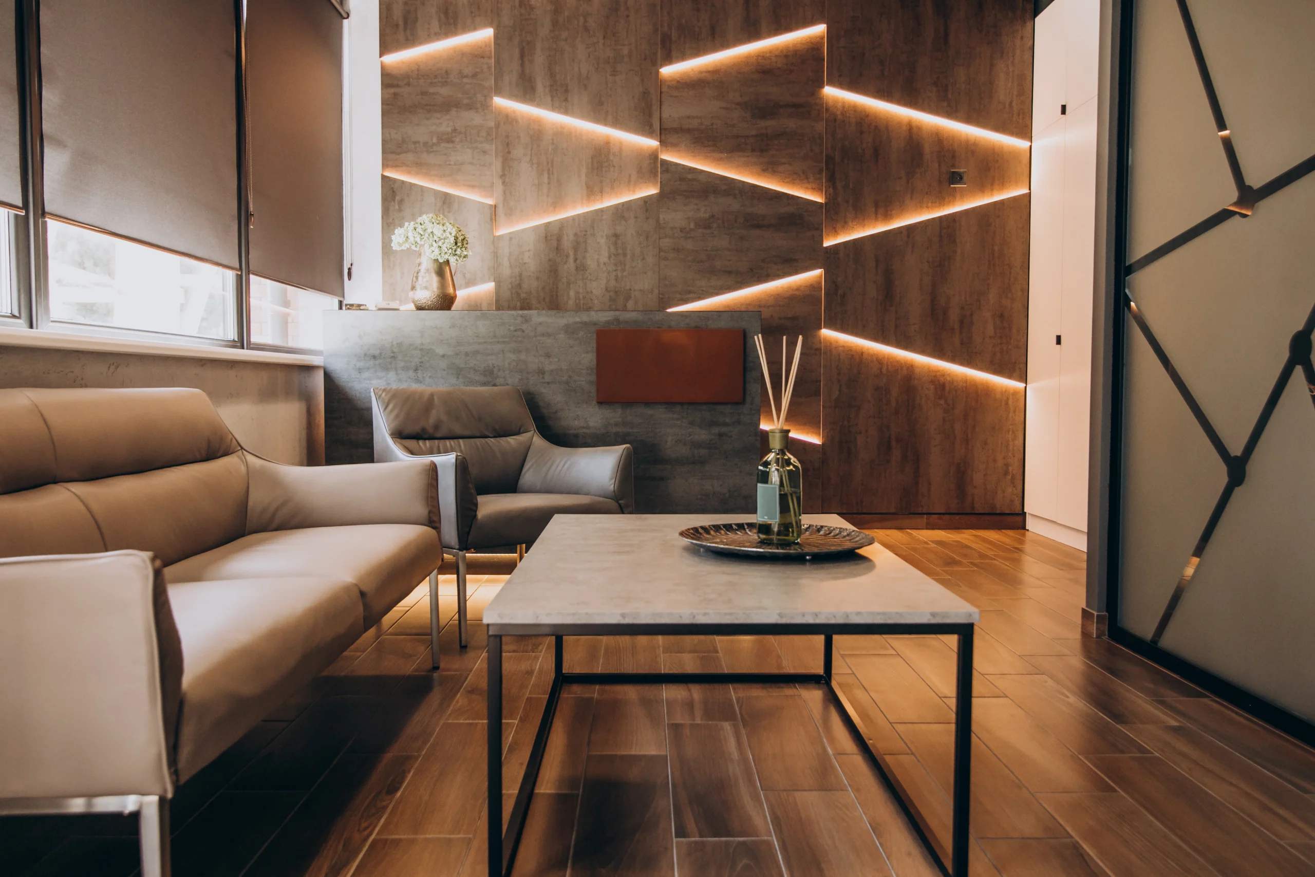 Contemporary lounge area featuring a tan leather sofa, coffee table, and an accent wall with integrated LED lighting.