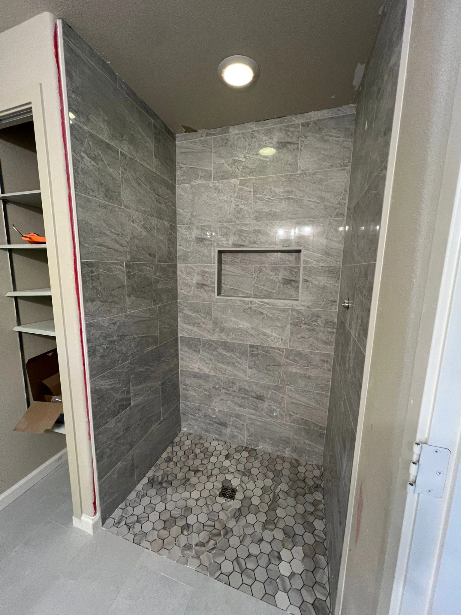 A modern tiled shower with gray walls, hexagon floor, and a shelf, perfect for an Interior Remodeling Project.
